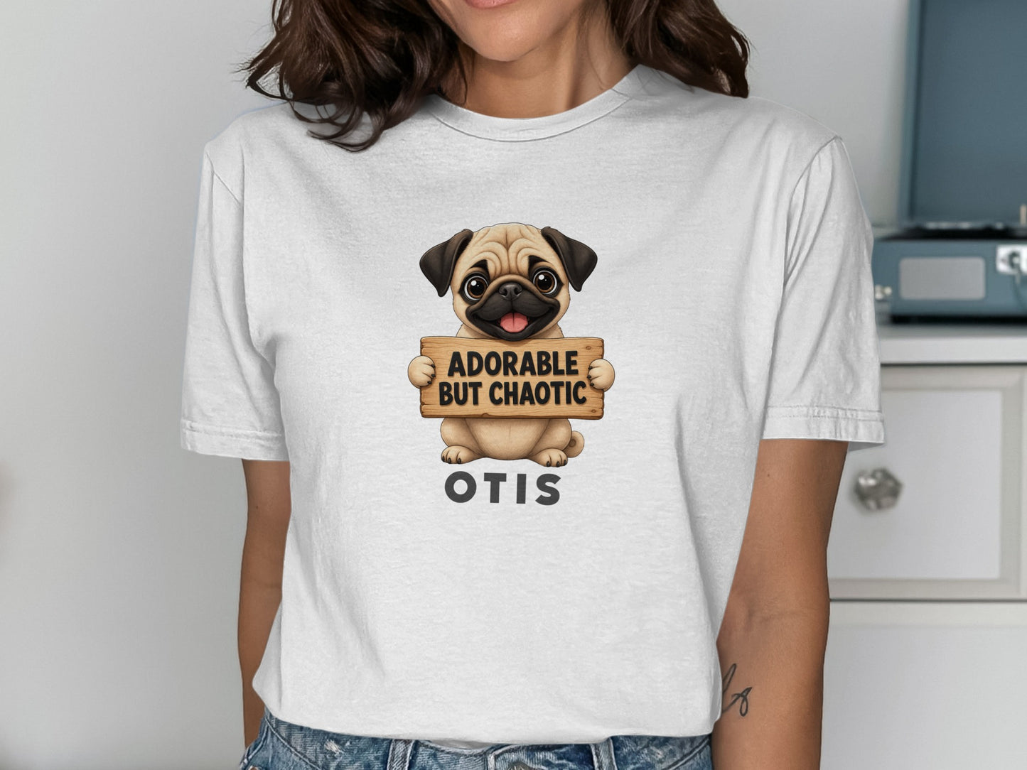 White t-shirt with a pug holding a sign that says "ADORABLE BUT CHAOTIC OTIS".