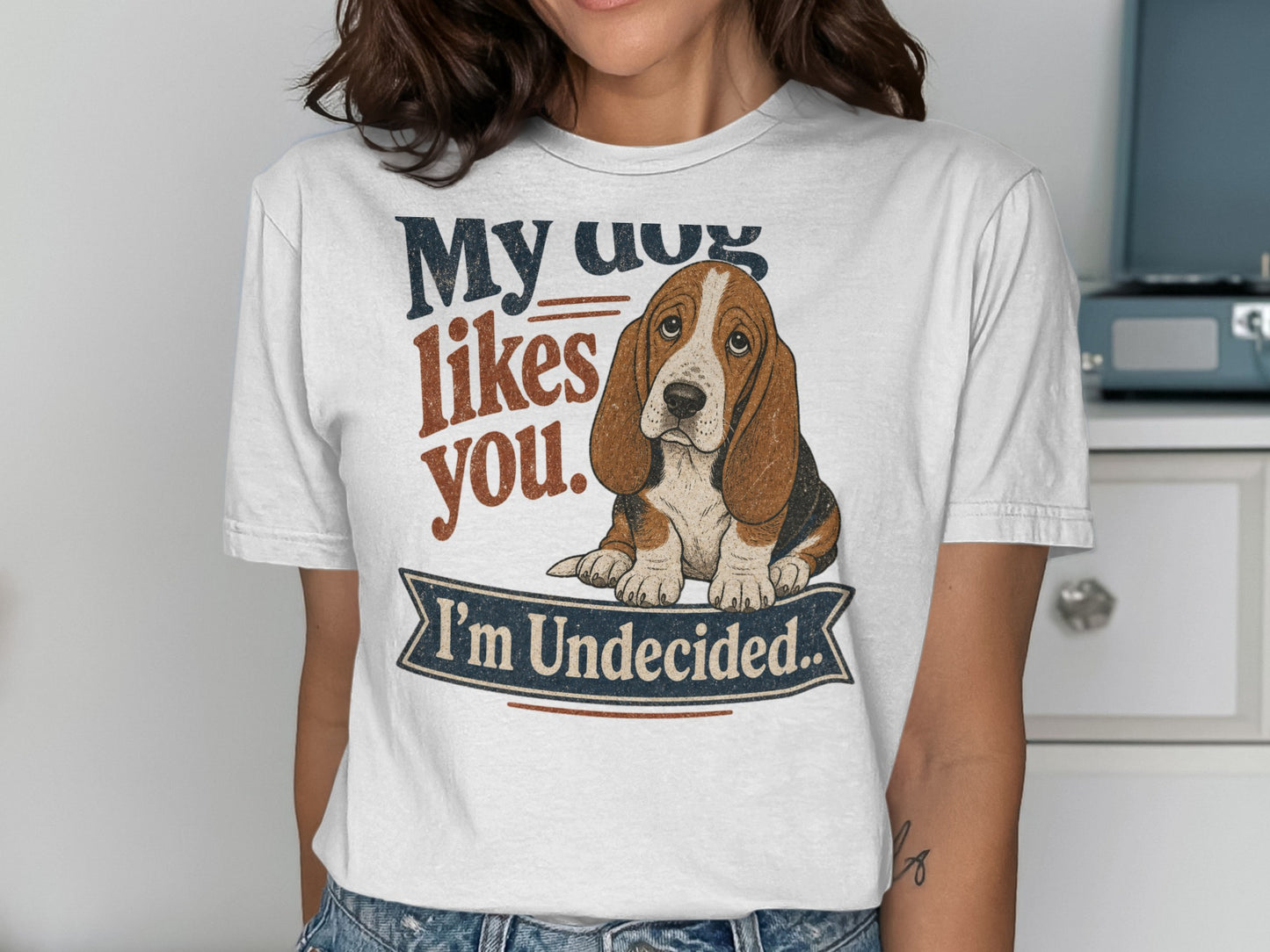 White t-shirt with a Basset Hound graphic and text "My dog likes you. I'm Undecided.".