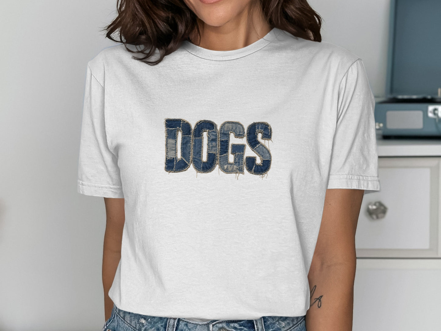 White t-shirt with "DOGS" spelled out in distressed denim patches.