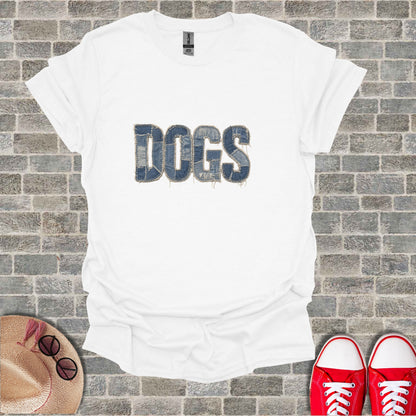 White t-shirt with "DOGS" text in denim-texture, laid flat with hat and sneakers.