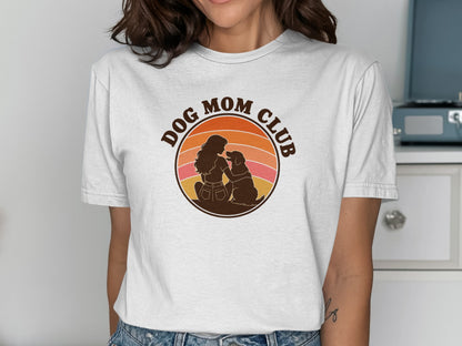 White t-shirt graphic with a silhouette of a woman and dog within a retro sunset circle that reads "DOG MOM CLUB."