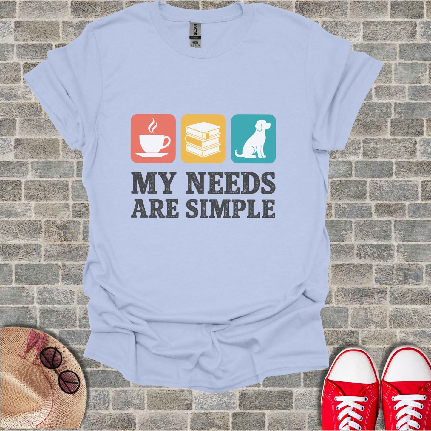 Light blue t-shirt with coffee, books, and dog icons and the text "MY NEEDS ARE SIMPLE".