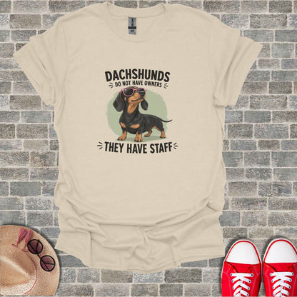 Dachshund with sunglasses on beige t-shirt that says "Dachshunds do not have owners they have staff".