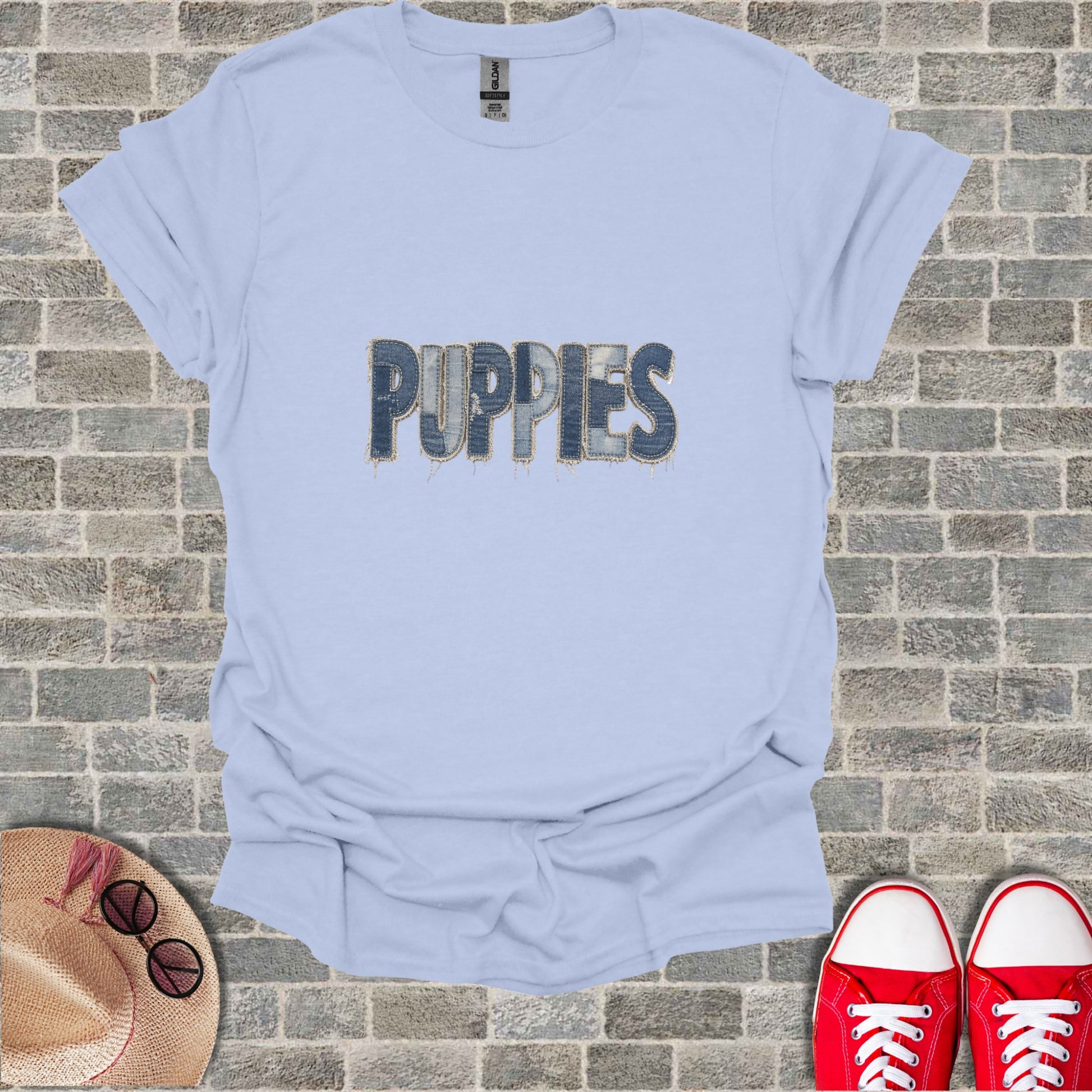 Light blue t-shirt with distressed denim "PUPPIES" graphic on a brick background.