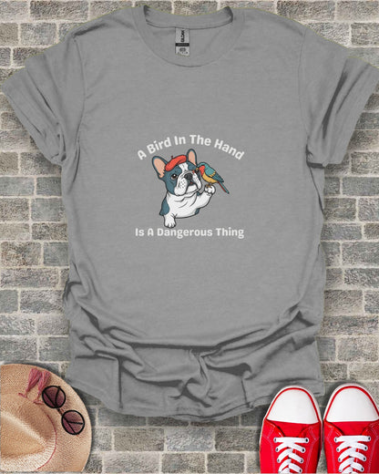 French bulldog holding a bird on its paw with text "A Bird In The Hand Is A Dangerous Thing."