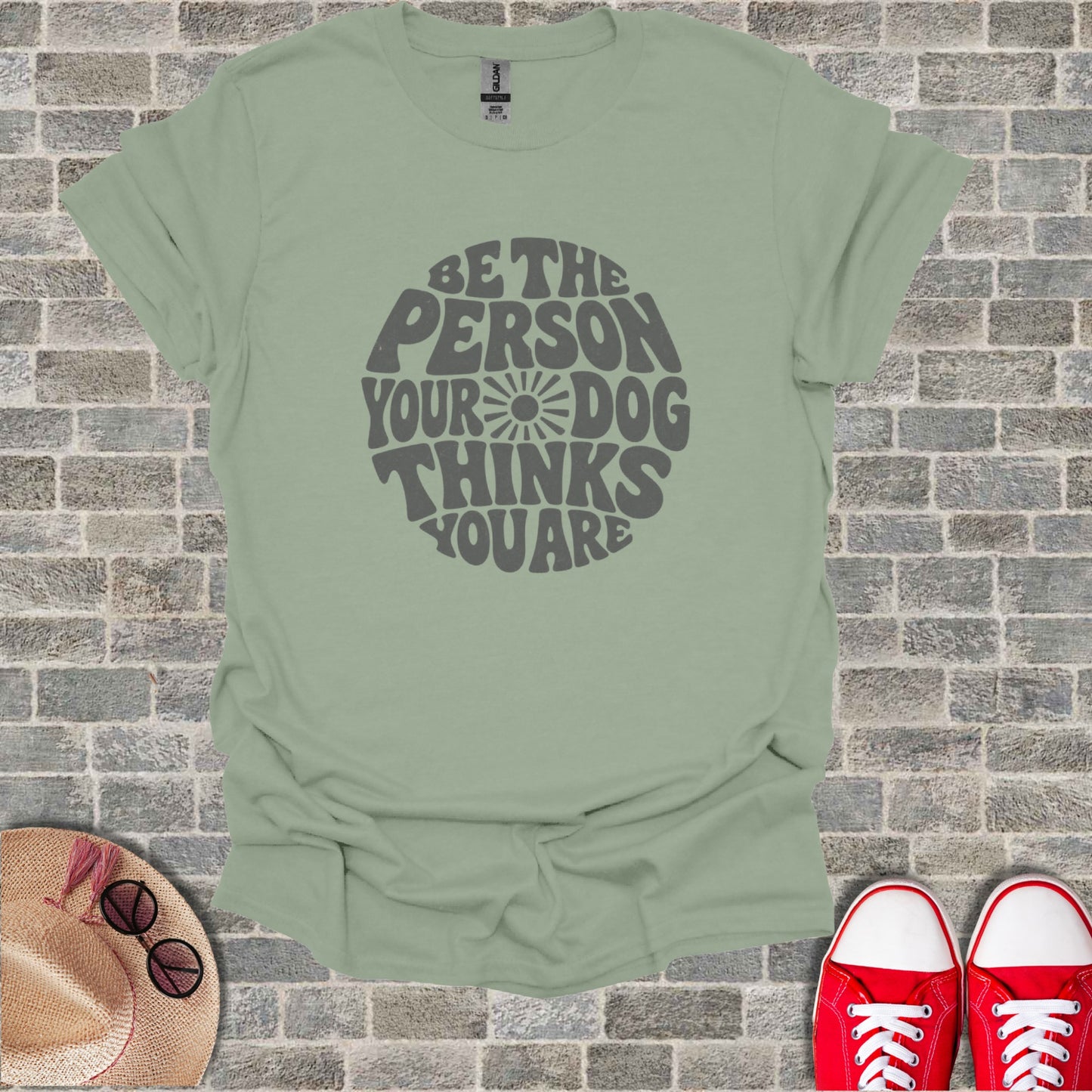 A sage green t-shirt with the text "Be the person your dog thinks you are"