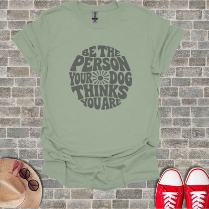 A sage green t-shirt with the text "Be the person your dog thinks you are"