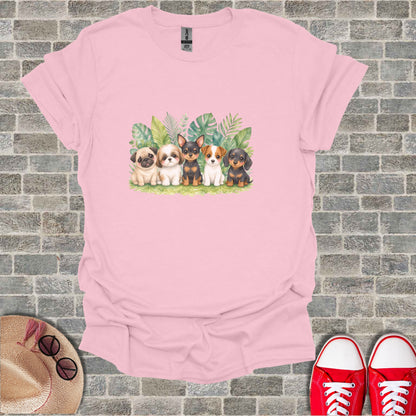 Five puppies sitting in front of lush green foliage on a pink t-shirt.