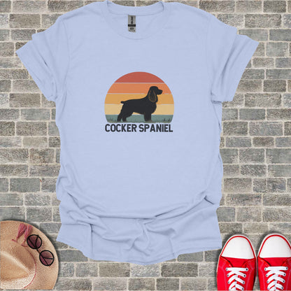 Light blue t-shirt with black cocker spaniel silhouette and sunset graphic.