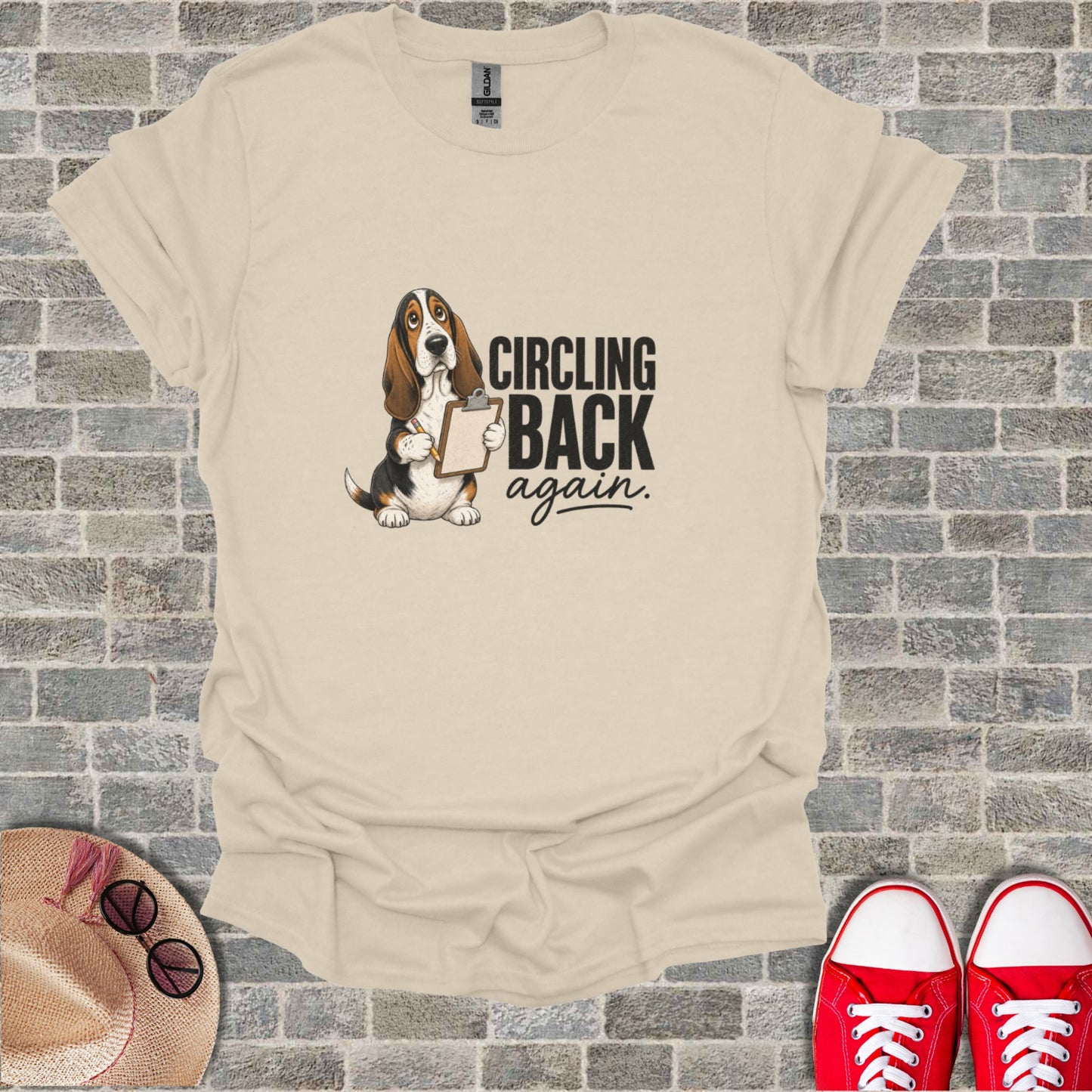 Basset hound with clipboard says "Circling back again" on a cream t-shirt.