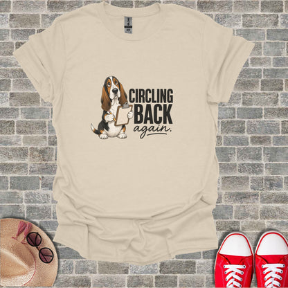Basset hound with clipboard says "Circling back again" on a cream t-shirt.