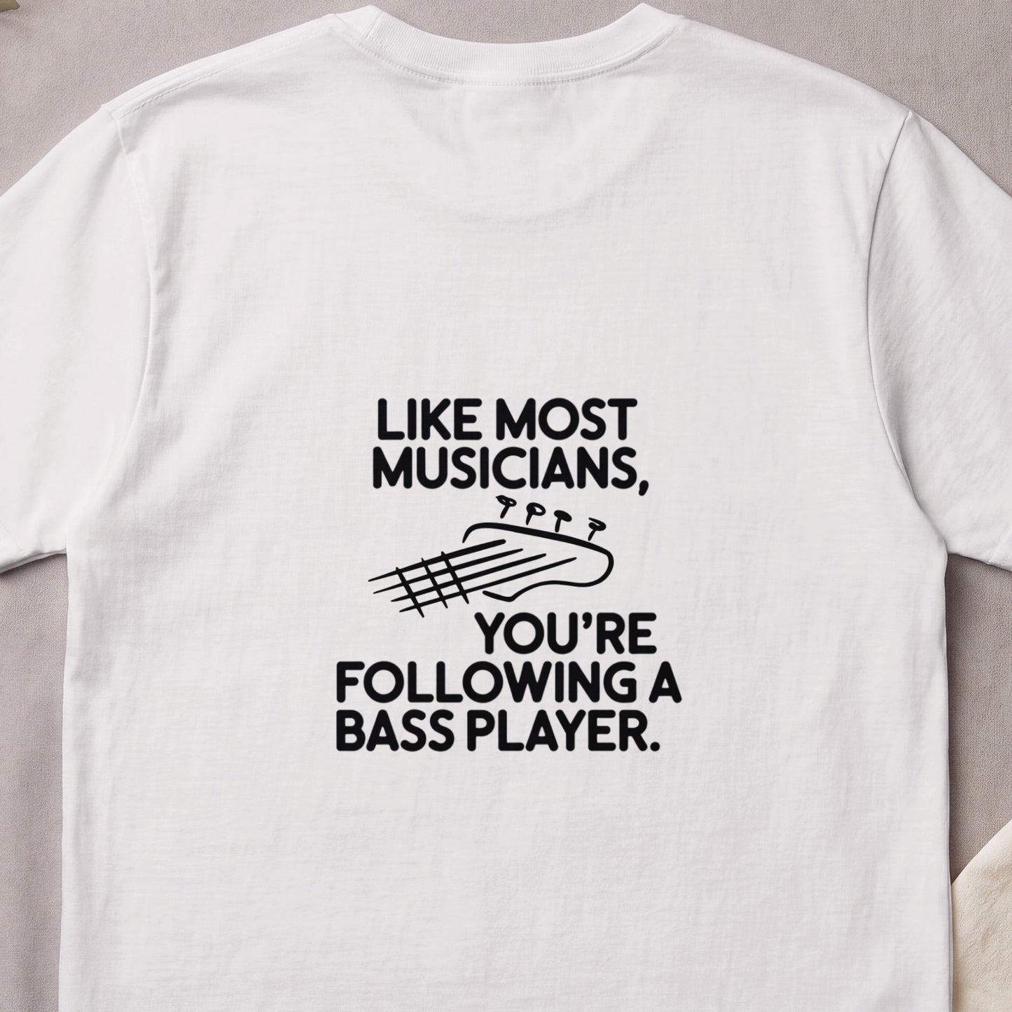 White t-shirt with text "Like Most Musicians, You're Following a Bass Player" and guitar headstock graphic.