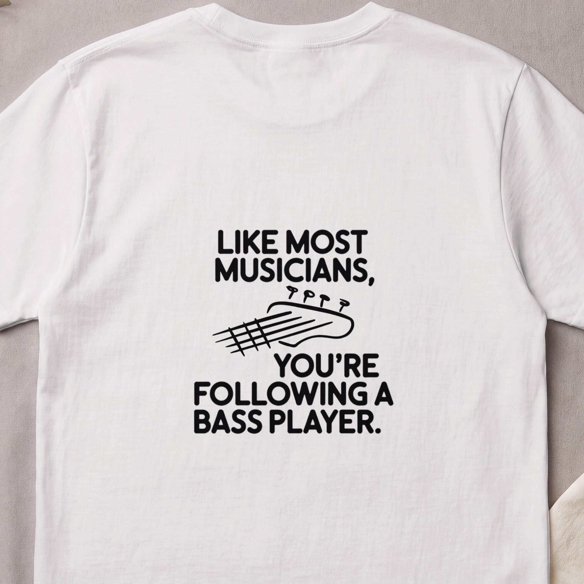 White t-shirt with text "Like Most Musicians, You're Following a Bass Player" and guitar headstock graphic.