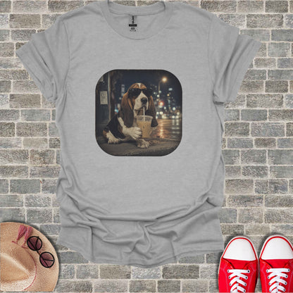Basset hound wearing sunglasses drinks from a to-go cup at night.