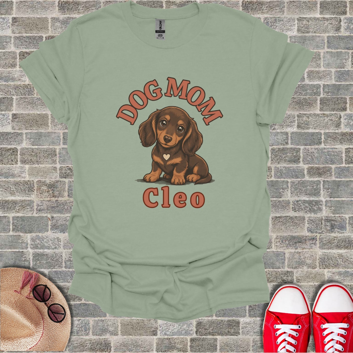 Dachshund dog with "DOG MOM CLEO" text on a light green t-shirt.