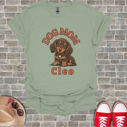 Dachshund dog with "DOG MOM CLEO" text on a light green t-shirt.