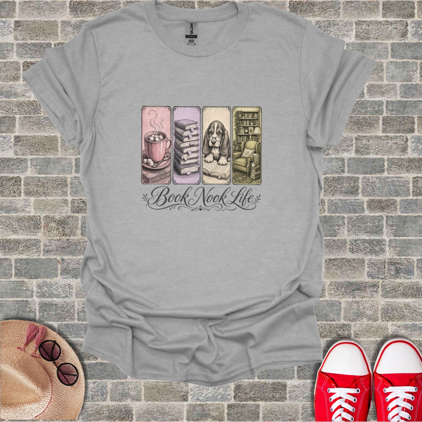 T-shirt with "Book Nook Life" text and four illustrated scenes: hot chocolate, books, armchair, and cat.