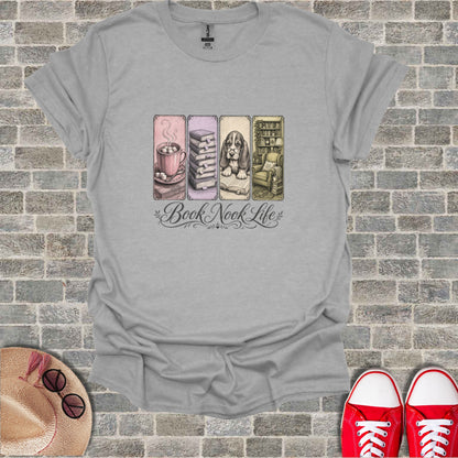 T-shirt with "Book Nook Life" text and four illustrated scenes: hot chocolate, books, armchair, and cat.