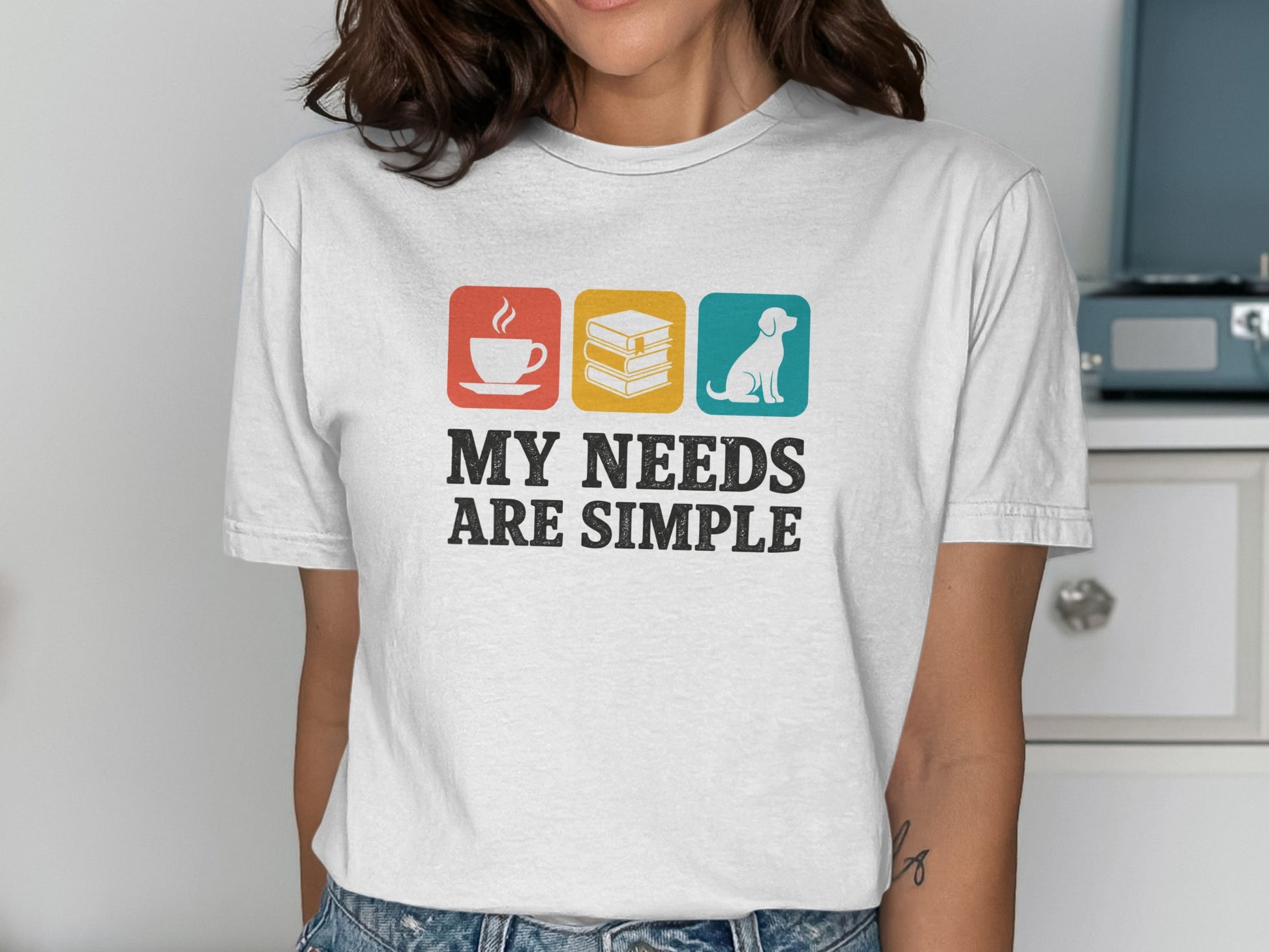 White t-shirt with icons for coffee, books, dog and text "MY NEEDS ARE SIMPLE".