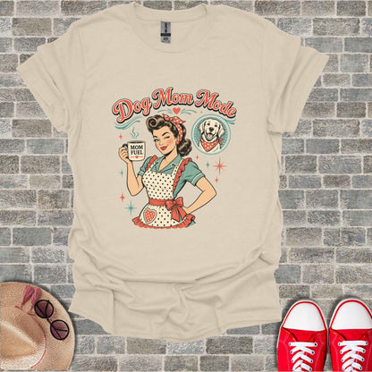 "Dog Mom Mode" graphic on a cream t-shirt with a retro woman holding "MOM FUEL" mug.