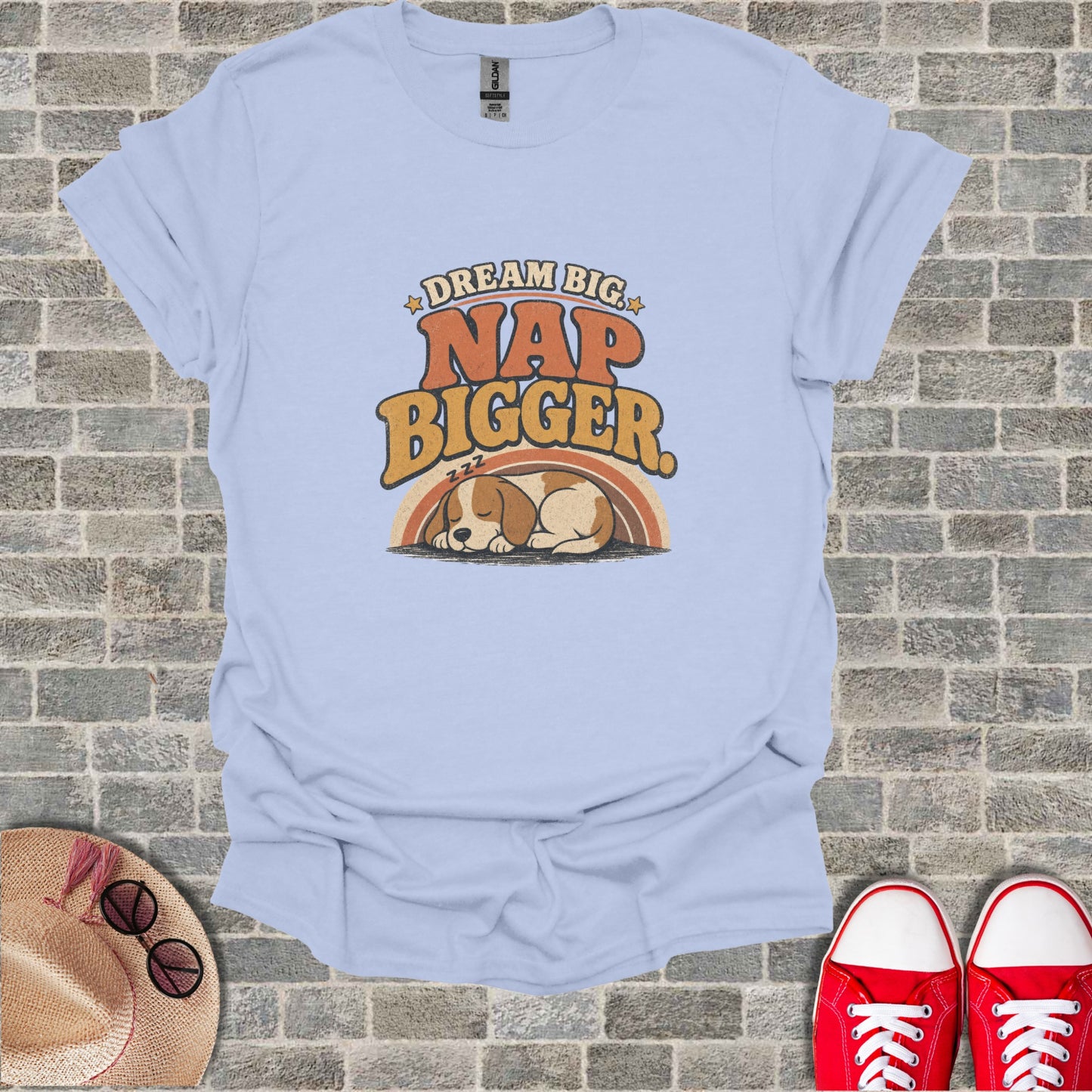 Light blue t-shirt with dog sleeping under rainbow and text "Dream Big Nap Bigger".