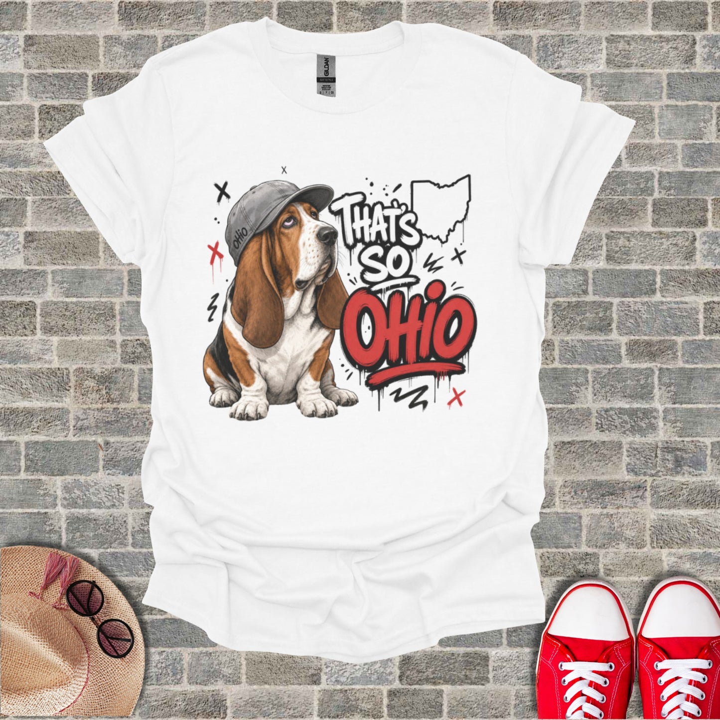 Basset hound wearing a hat sits on a white t-shirt with "That's So Ohio" graphic.
