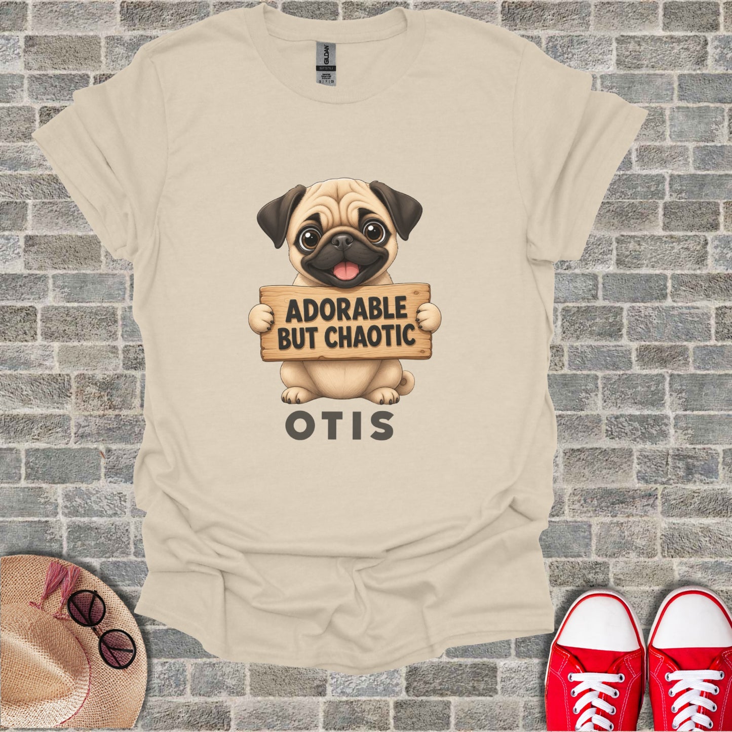 Cream t-shirt with a pug graphic holding a sign that says "Adorable But Chaotic Otis".