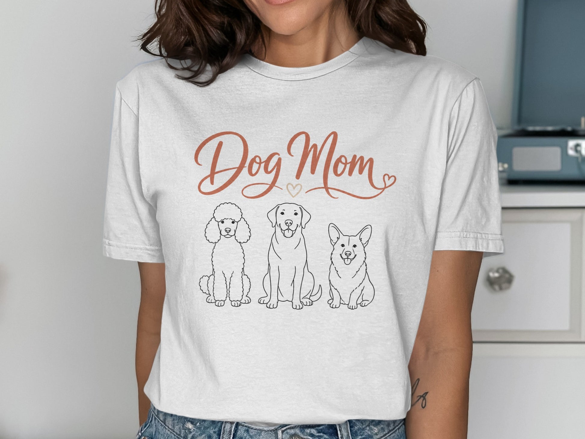 White t-shirt with "Dog Mom" text and line drawings of a poodle, labrador, and corgi.