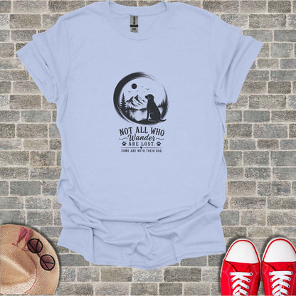 Light blue t-shirt with black silhouette of dog, mountains, and trees. Text reads "Not All Who Wander Are Lost. Some Are With Their Dog."