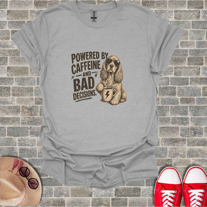 Gray t-shirt with sketch of a dog holding a coffee cup, text reads "POWERED BY CAFFEINE AND BAD DECISIONS."