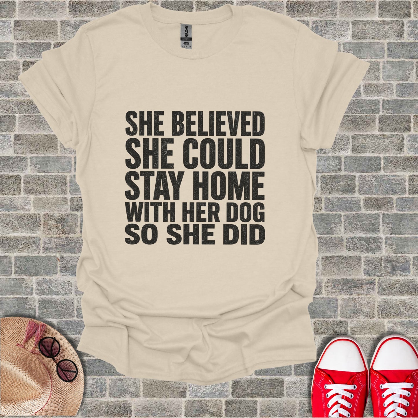 Light beige t-shirt with black text "She believed she could stay home with her dog so she did."