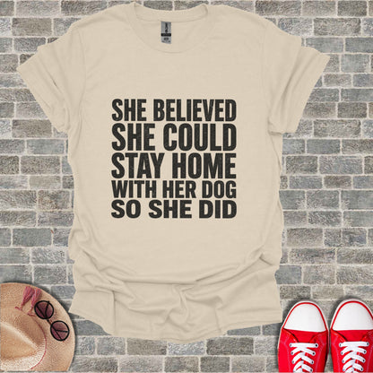 Light beige t-shirt with black text "She believed she could stay home with her dog so she did."