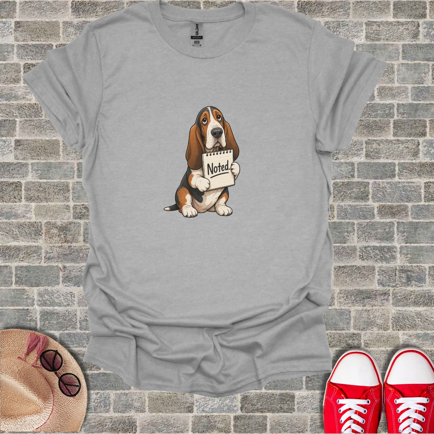 Basset hound wearing a t-shirt holds a sign that says "Noted."