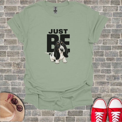 Basset hound illustration with "JUST BE" text on a pale green t-shirt.