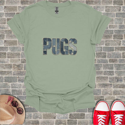 Green t-shirt with "PUGS" in denim patches on a brick wall background.