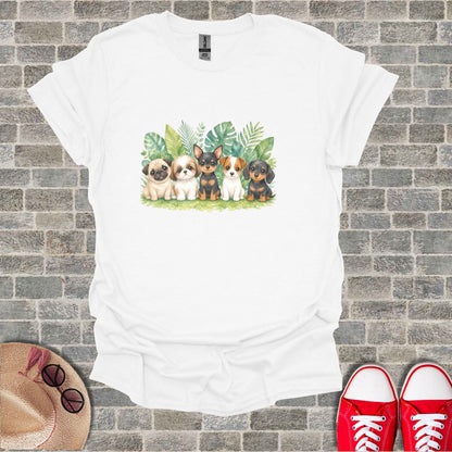 Five puppies sit in front of lush green foliage on a white t-shirt.