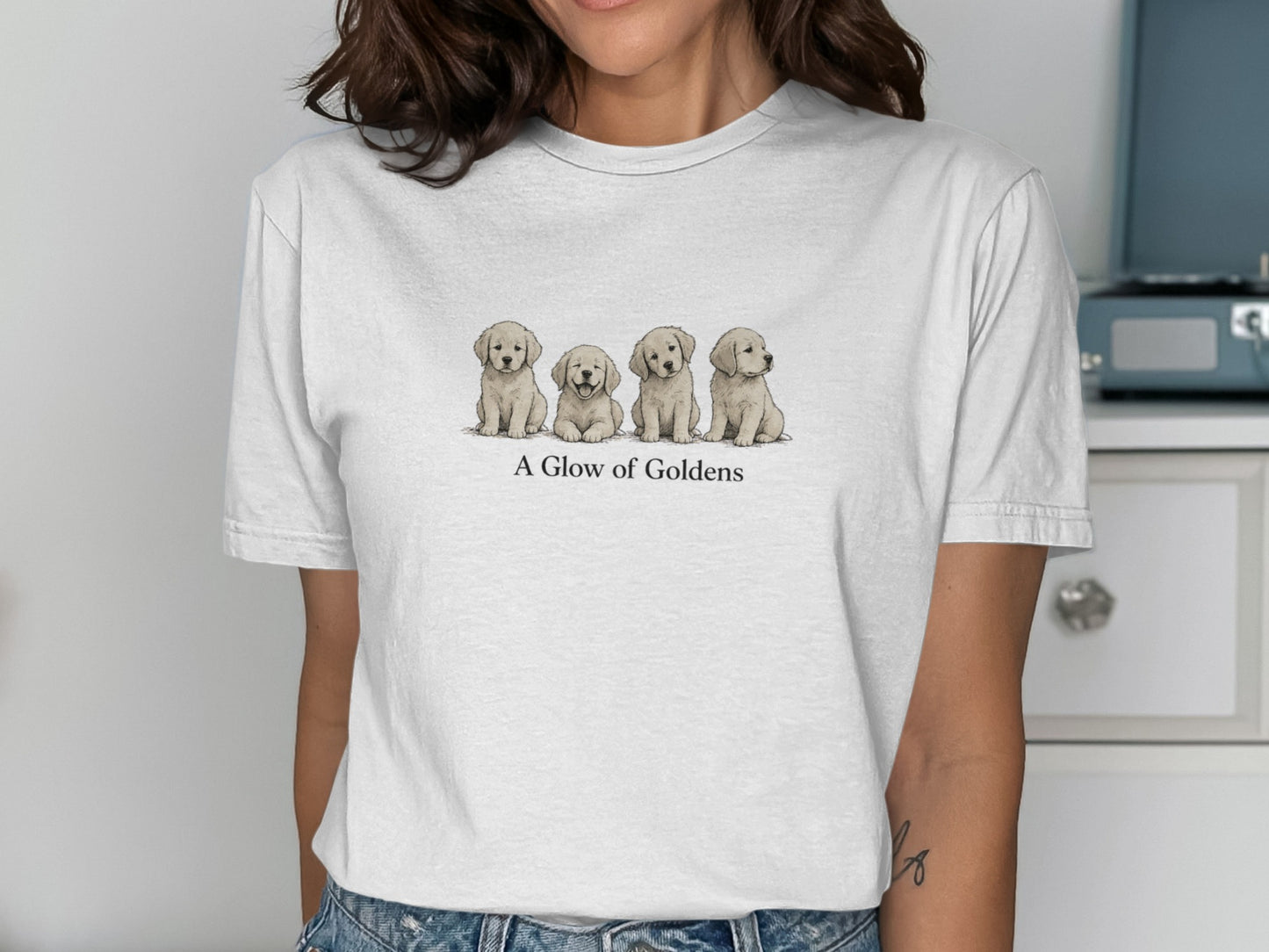 Four golden retriever puppies sit in a row on a white t-shirt.