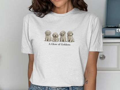 Four golden retriever puppies sit in a row on a white t-shirt.