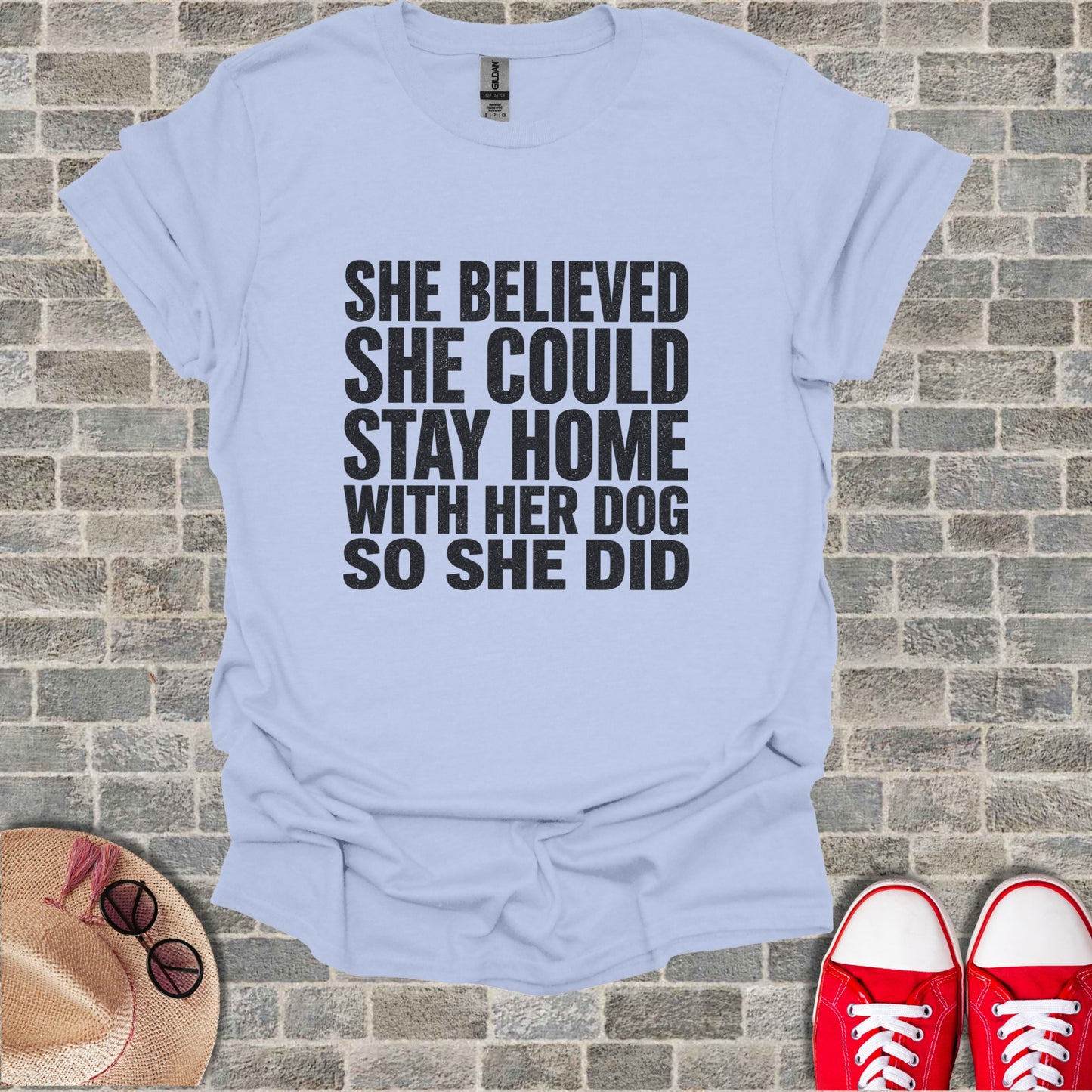 Light blue t-shirt with text "She believed she could stay home with her dog so she did."