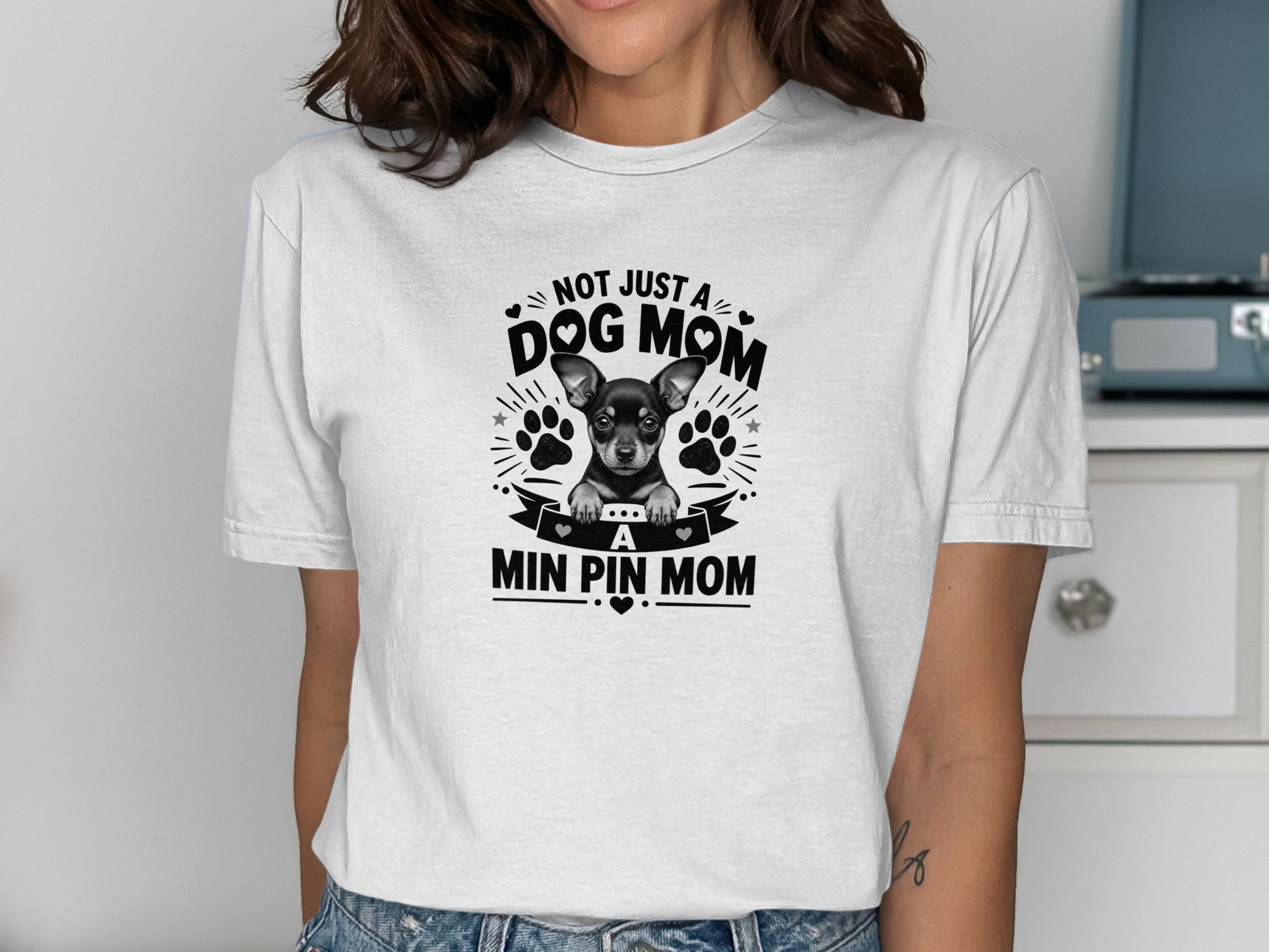 White t-shirt with black graphic showing a mini pinscher dog and text "NOT JUST A DOG MOM, A MIN PIN MOM".