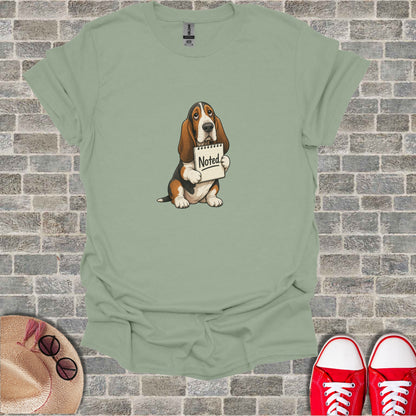 Basset hound holding a "Noted" sign with distressed expression.
