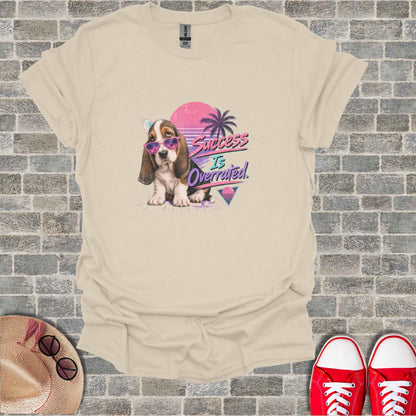 Light tan t-shirt with graphic of a dog wearing sunglasses and text "Success Is Overrated."