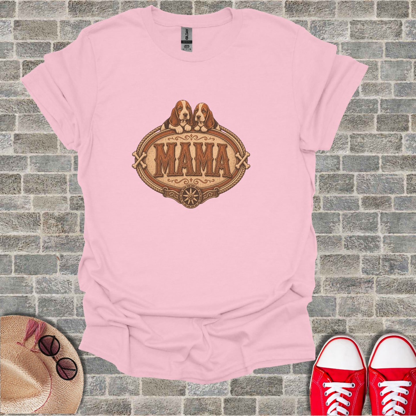 Pink t-shirt with "MAMA" and dog illustration, on a brick background.