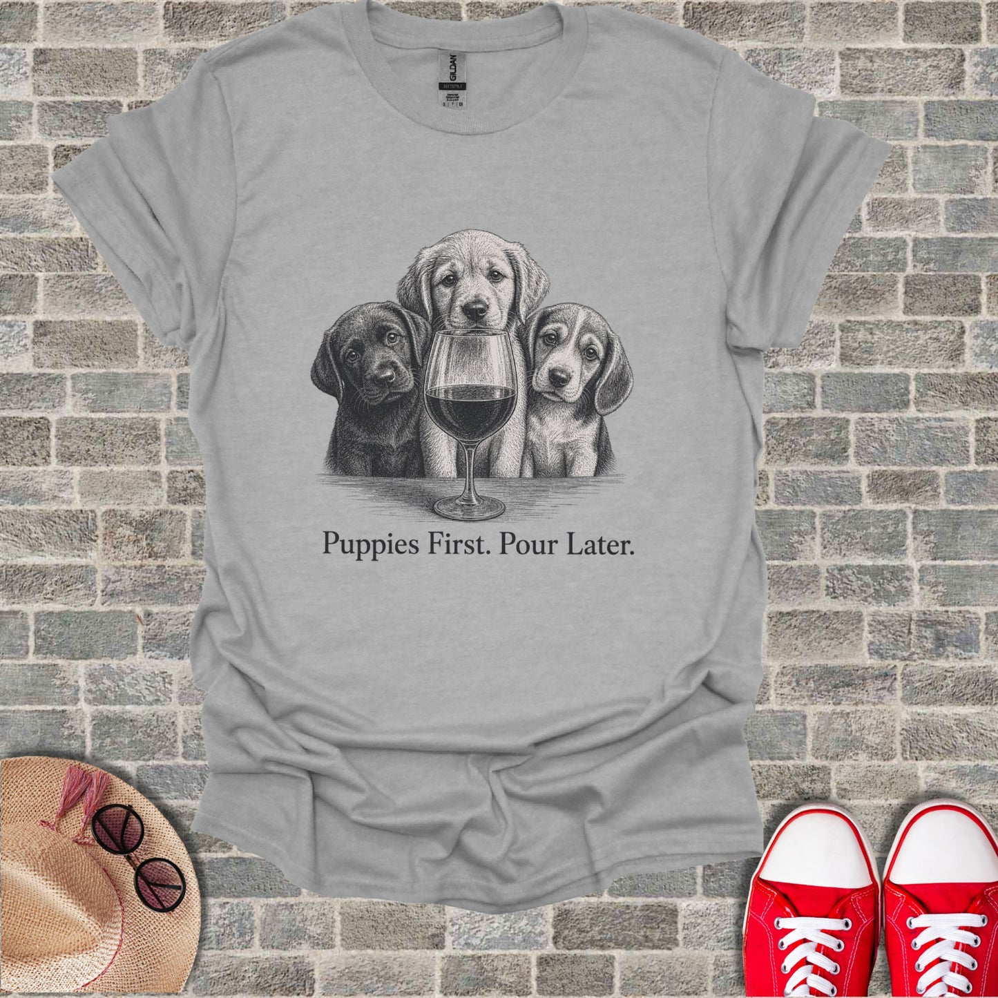Three puppies peer over a wine glass on a gray t-shirt with text.