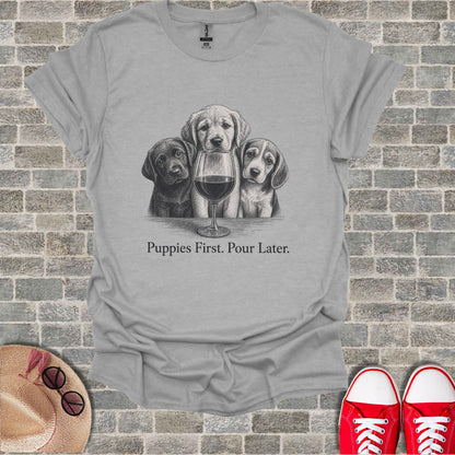 Three puppies peer over a wine glass on a gray t-shirt with text.