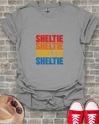 Gray t-shirt with "SHELTIE" printed four times in colorful block letters.