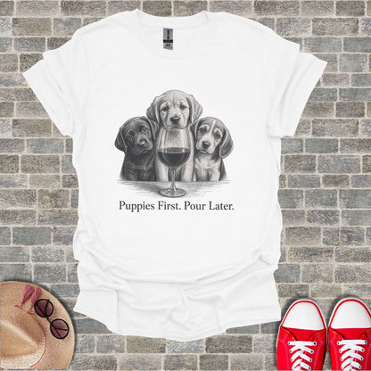 White t-shirt with three puppies and a wine glass, saying "Puppies First. Pour Later."