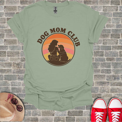 Green t-shirt with a circular graphic of a woman and dog under a sunset and "DOG MOM CLUB" text.