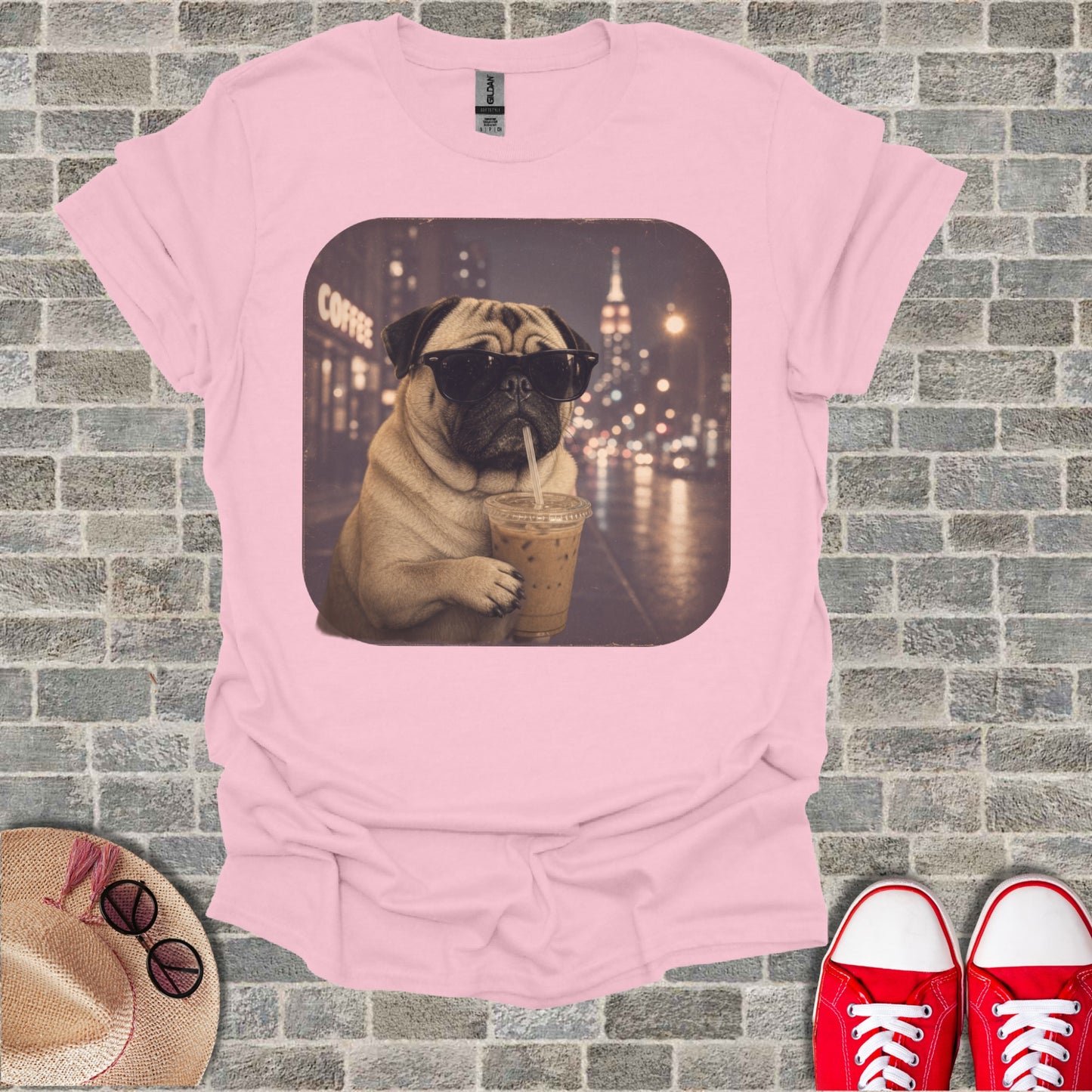 Pink t-shirt with a pug wearing sunglasses drinking iced coffee on a city street.