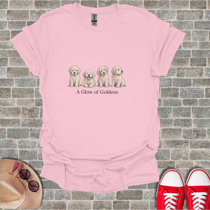 Pink t-shirt with illustration of four golden retriever puppies and text "A Glow of Goldens".